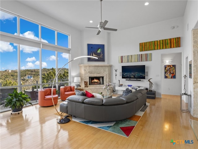 living area with ceiling fan, hardwood / wood-style floors, recessed lighting, a fireplace, and a towering ceiling