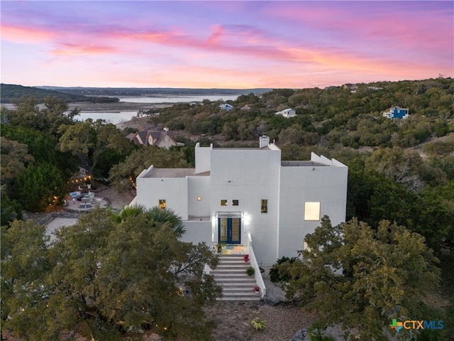 aerial view at dusk featuring a view of trees and a water view