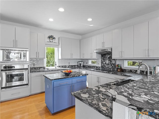 kitchen with a kitchen island, dark stone counters, stainless steel appliances, light wood-style floors, and under cabinet range hood