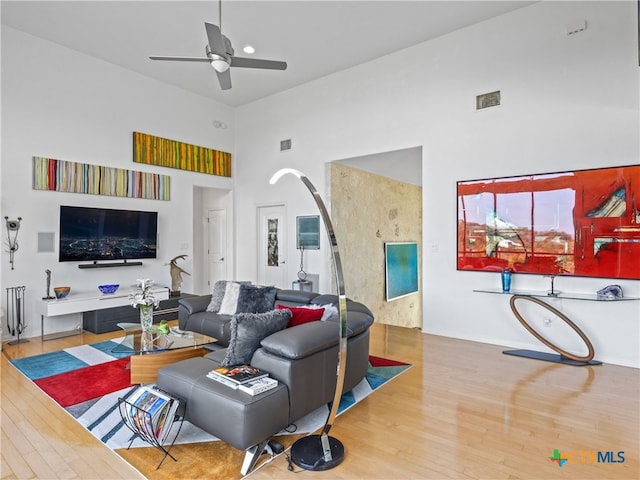 living room featuring wood finished floors, visible vents, a high ceiling, arched walkways, and ceiling fan