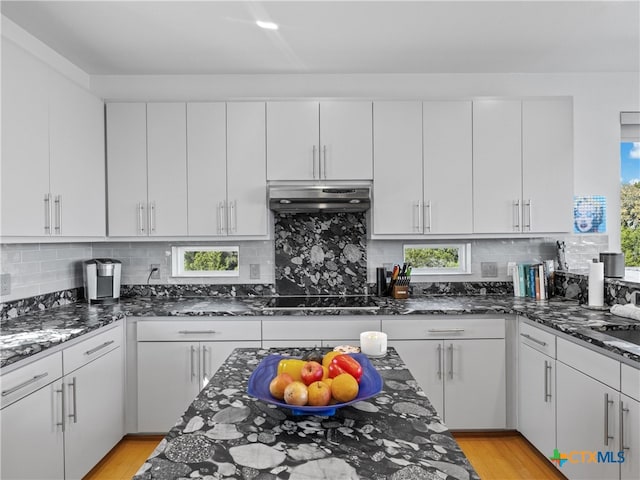 kitchen with under cabinet range hood, dark stone countertops, black electric cooktop, and backsplash