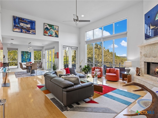 living area featuring a stone fireplace, a healthy amount of sunlight, a ceiling fan, and hardwood / wood-style flooring