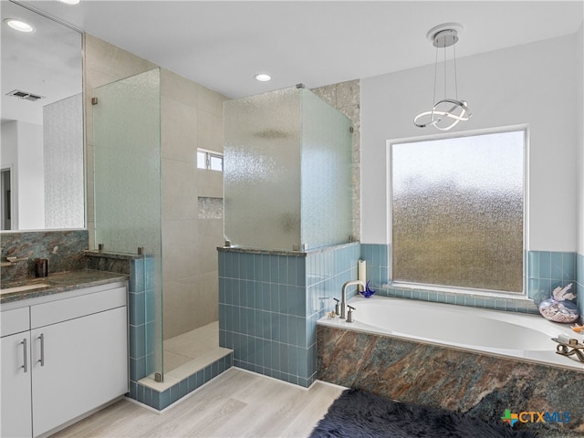 bathroom featuring visible vents, a walk in shower, wood finished floors, a bath, and vanity