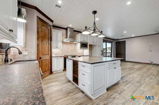 kitchen featuring wall chimney range hood, crown molding, a sink, stainless steel microwave, and visible vents