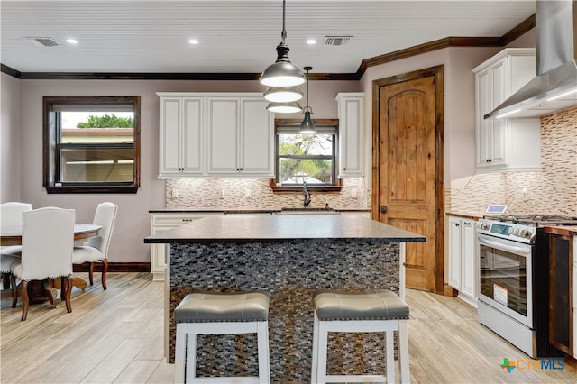 kitchen with wall chimney exhaust hood, stainless steel range with gas stovetop, a sink, and a healthy amount of sunlight