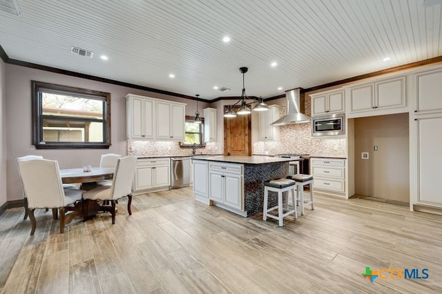 kitchen featuring wall chimney range hood, crown molding, stainless steel appliances, backsplash, and a kitchen island