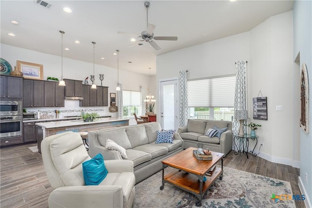 living area with visible vents, baseboards, wood tiled floor, ceiling fan with notable chandelier, and recessed lighting