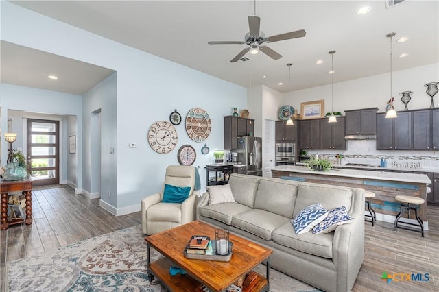 living room with light wood-style floors, visible vents, baseboards, and a ceiling fan