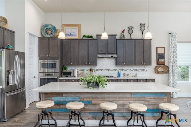 kitchen with hanging light fixtures, a center island with sink, stainless steel appliances, and light countertops