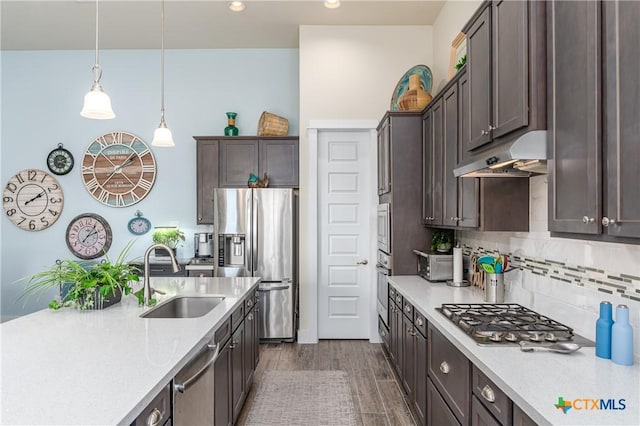 kitchen with dark wood-style flooring, stainless steel appliances, hanging light fixtures, a sink, and under cabinet range hood