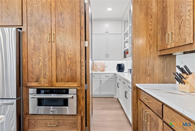 kitchen featuring white cabinetry, appliances with stainless steel finishes, light stone counters, and light hardwood / wood-style flooring