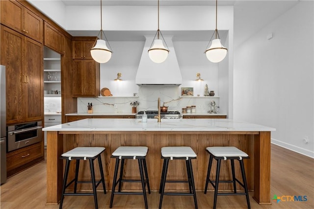 kitchen with a breakfast bar area, premium range hood, tasteful backsplash, stainless steel oven, and light wood-type flooring