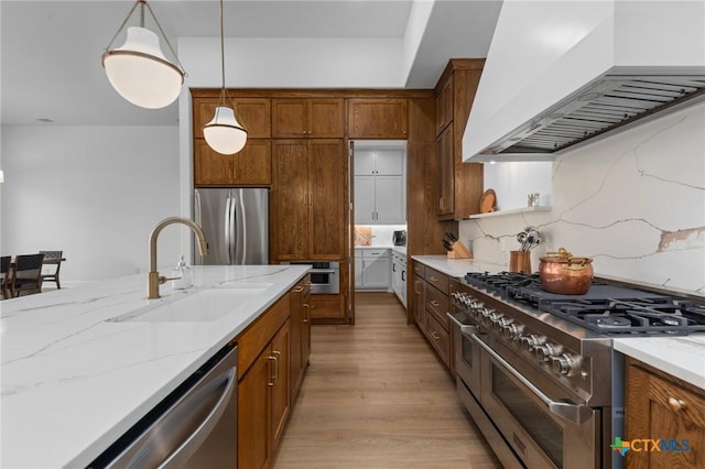 kitchen featuring premium range hood, sink, hanging light fixtures, light hardwood / wood-style floors, and stainless steel appliances