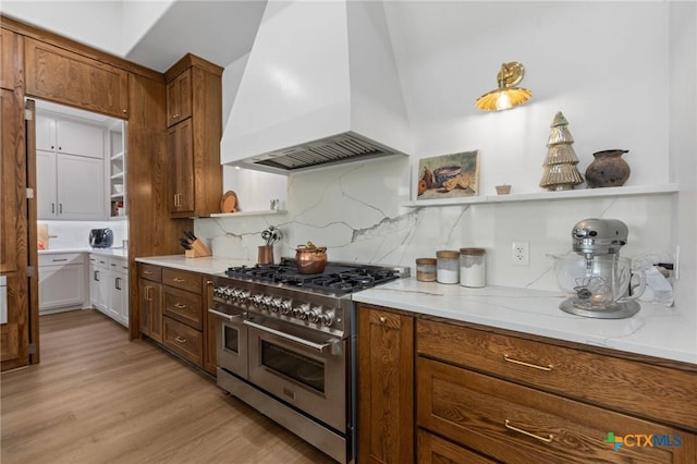 kitchen with double oven range, custom range hood, backsplash, and light wood-type flooring