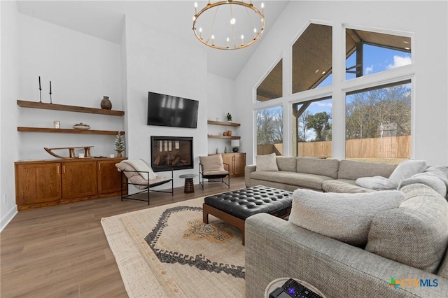 living room with high vaulted ceiling, a chandelier, and light wood-type flooring