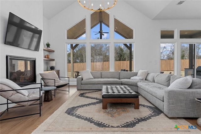 living room featuring a notable chandelier, a towering ceiling, light wood-type flooring, and a wealth of natural light