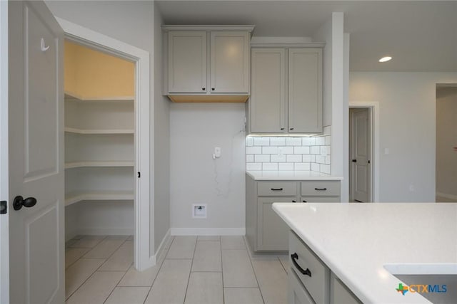 kitchen with light tile patterned floors, tasteful backsplash, light countertops, gray cabinetry, and baseboards