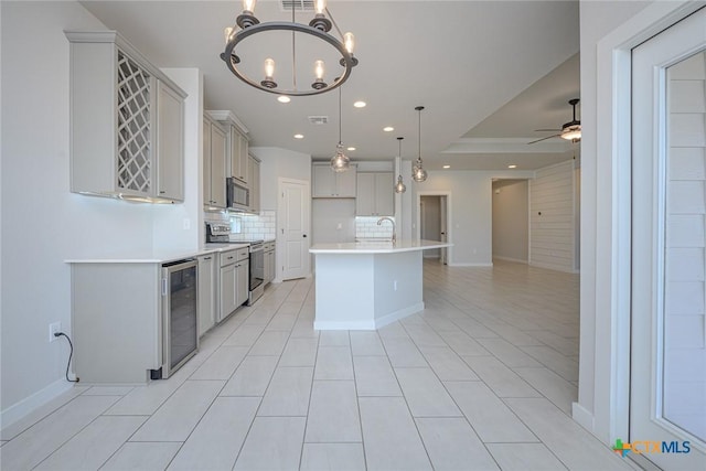 kitchen with decorative backsplash, wine cooler, appliances with stainless steel finishes, a sink, and ceiling fan with notable chandelier