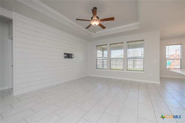 spare room with baseboards, a ceiling fan, a tray ceiling, crown molding, and wood walls