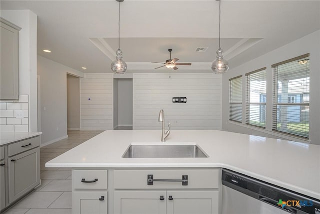 kitchen featuring dishwasher, decorative light fixtures, a tray ceiling, light countertops, and a sink