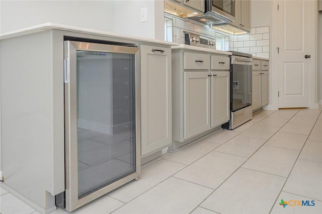 kitchen featuring beverage cooler, light countertops, backsplash, and light tile patterned floors