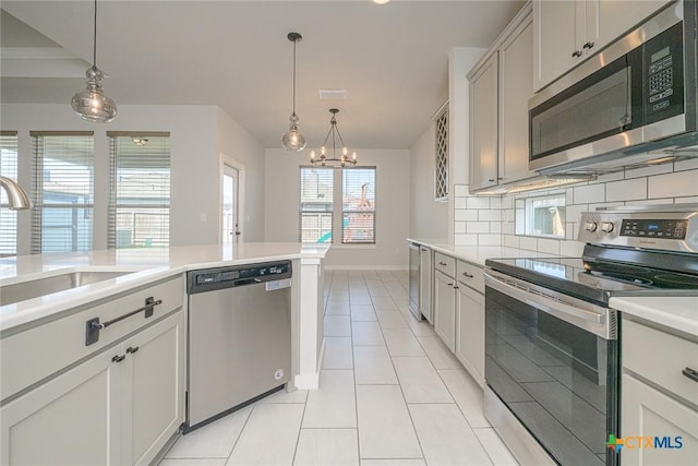 kitchen featuring light tile patterned floors, appliances with stainless steel finishes, decorative light fixtures, light countertops, and backsplash