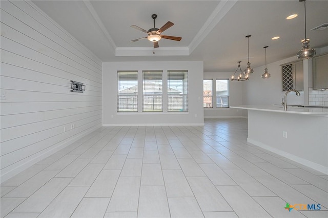 unfurnished living room featuring ceiling fan, visible vents, baseboards, a raised ceiling, and crown molding