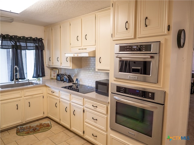 kitchen featuring light tile patterned flooring, sink, black appliances, a textured ceiling, and decorative backsplash