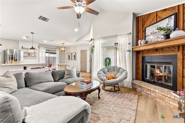 living room with visible vents, vaulted ceiling, light wood finished floors, a brick fireplace, and a ceiling fan