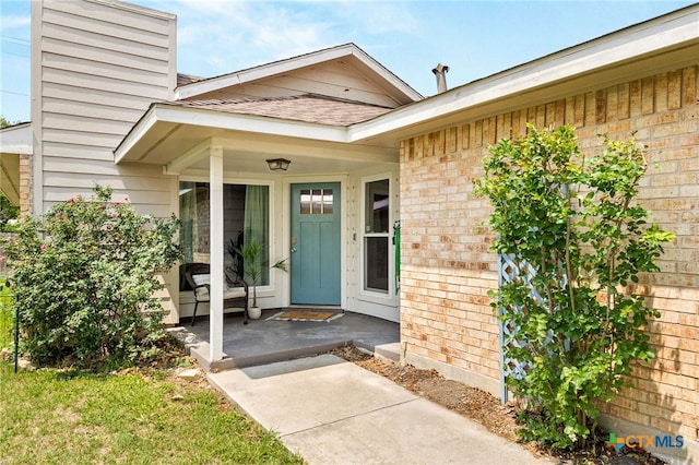 doorway to property with a porch, roof with shingles, and brick siding
