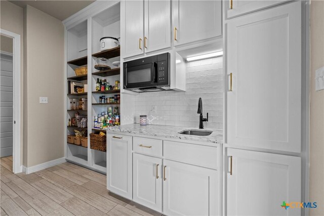 813 Reston Rd, Temple, TX 76502 - kitchen with black microwave, open shelves, backsplash, light stone counters, and light wood-type flooring