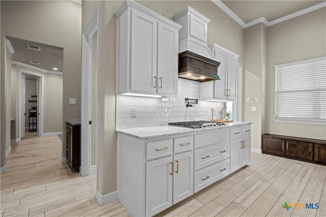 813 Reston Rd, Temple, TX 76502 - kitchen with stainless steel gas stovetop, ornamental molding, light wood-type flooring, white cabinetry, and light stone countertops
