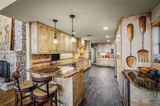 kitchen featuring wall chimney range hood, a breakfast bar area, hanging light fixtures, tasteful backsplash, and dark hardwood / wood-style flooring