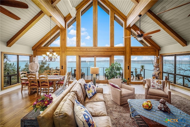 sunroom featuring lofted ceiling with beams, ceiling fan with notable chandelier, a water view, and a wealth of natural light