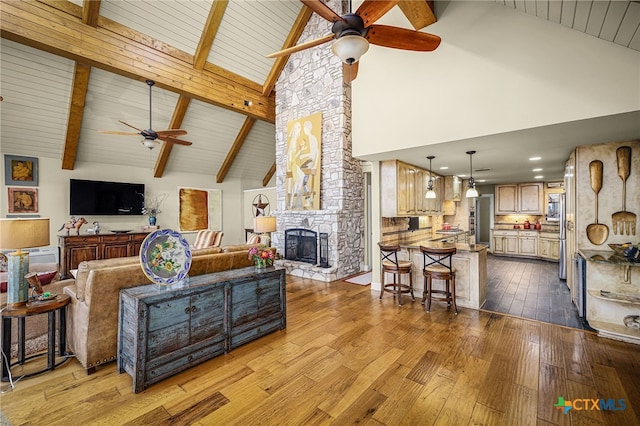 living room featuring beam ceiling, ceiling fan, a fireplace, and light hardwood / wood-style flooring