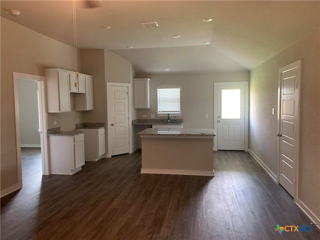 kitchen with dark wood-type flooring, a kitchen island, vaulted ceiling, and white cabinets