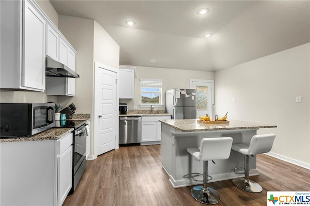 kitchen with appliances with stainless steel finishes, dark hardwood / wood-style floors, vaulted ceiling, white cabinets, and a center island