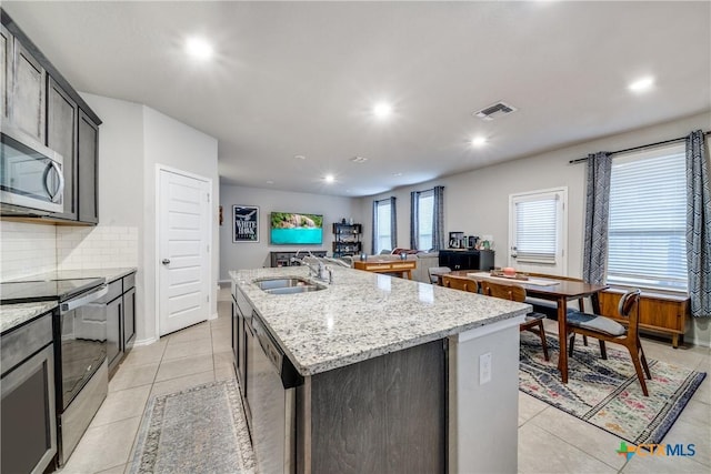 kitchen featuring sink, light tile patterned floors, a kitchen island with sink, stainless steel appliances, and light stone counters