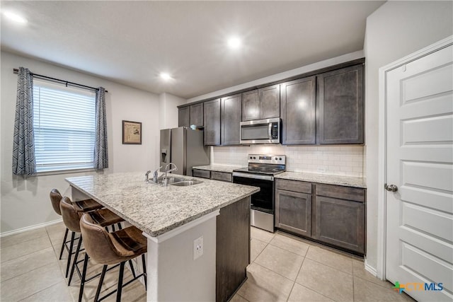 kitchen featuring tasteful backsplash, a center island with sink, light stone countertops, and appliances with stainless steel finishes