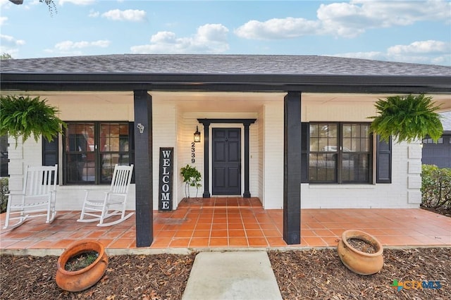 doorway to property featuring a porch and a shingled roof