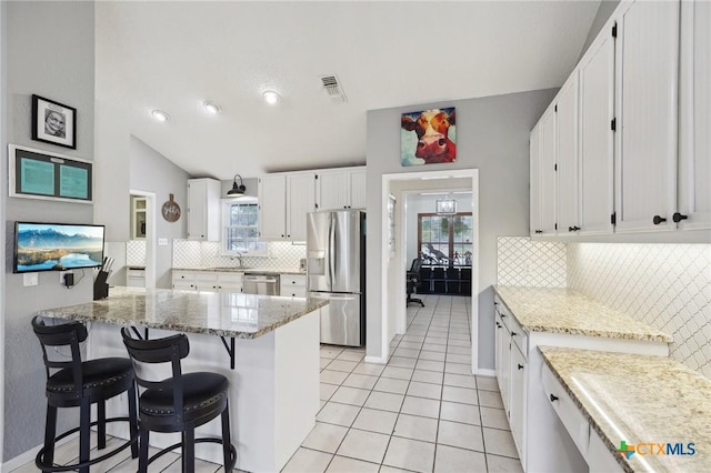 kitchen with a breakfast bar, white cabinets, light tile patterned floors, stainless steel appliances, and light stone countertops