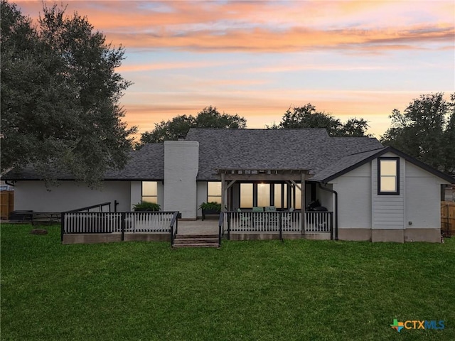 back house at dusk featuring a wooden deck and a lawn