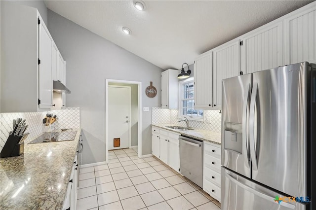 kitchen with vaulted ceiling, appliances with stainless steel finishes, white cabinetry, sink, and light stone countertops