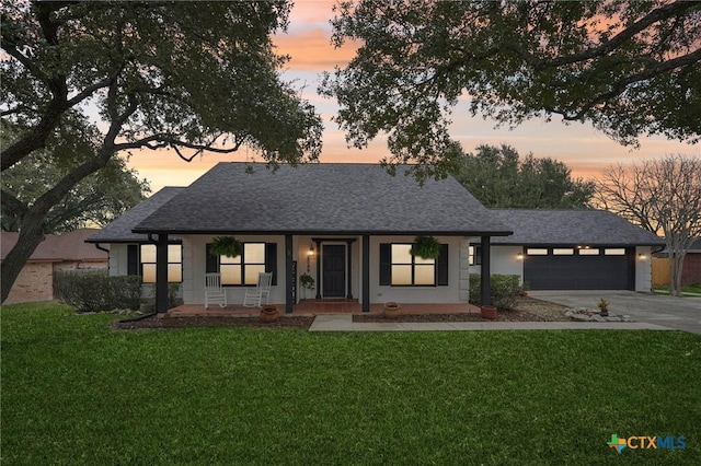 view of front facade with a shingled roof, covered porch, a lawn, driveway, and an attached garage