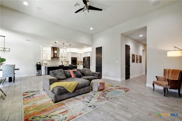 living room featuring ceiling fan with notable chandelier and light hardwood / wood-style flooring