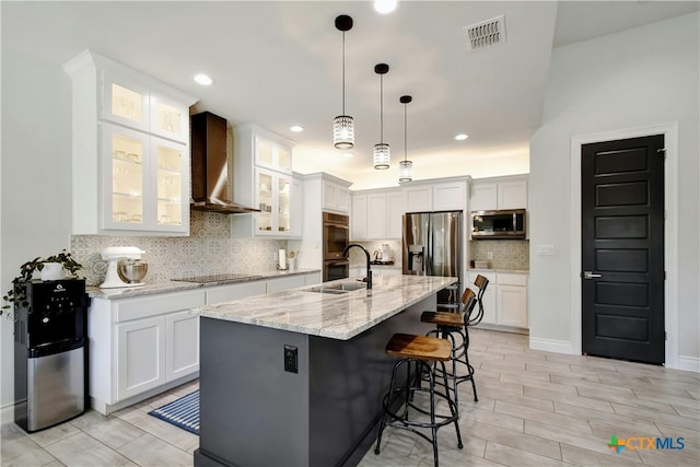 kitchen with white cabinetry, wall chimney range hood, appliances with stainless steel finishes, pendant lighting, and an island with sink