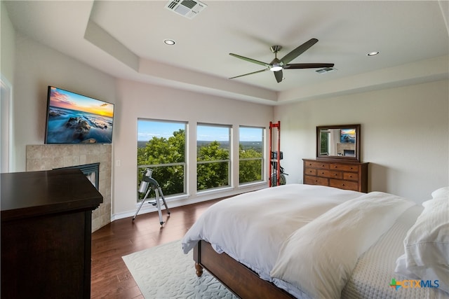 1280 Mystic Pkwy, Spring Branch, TX 78070 - bedroom with a tray ceiling, recessed lighting, dark wood-style flooring, a tile fireplace, and a ceiling fan
