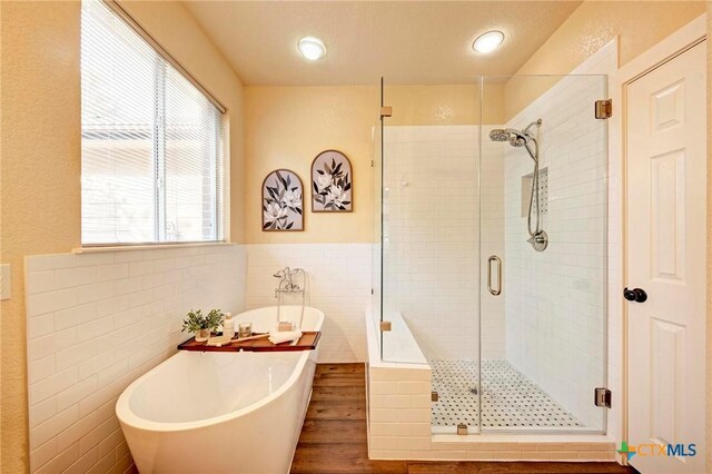 133 Ridgewood Cv, Georgetown, TX 78633 - bathroom with a shower stall, a soaking tub, wainscoting, tile walls, and wood finished floors