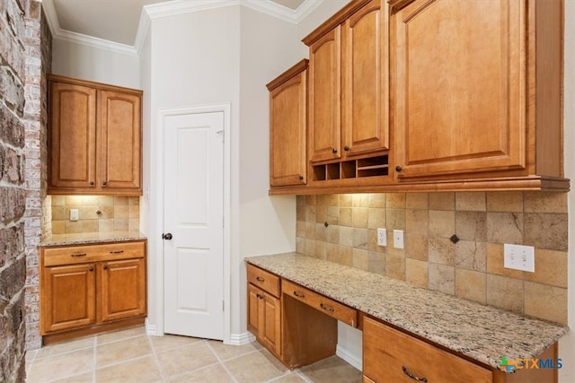 kitchen featuring built in desk, light stone counters, light tile patterned floors, backsplash, and crown molding