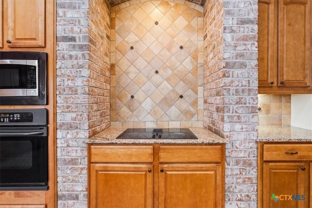 5909 Turtle Creek Trl, Temple, TX 76502 - kitchen with black appliances, light stone counters, brick wall, brown cabinets, and decorative backsplash
